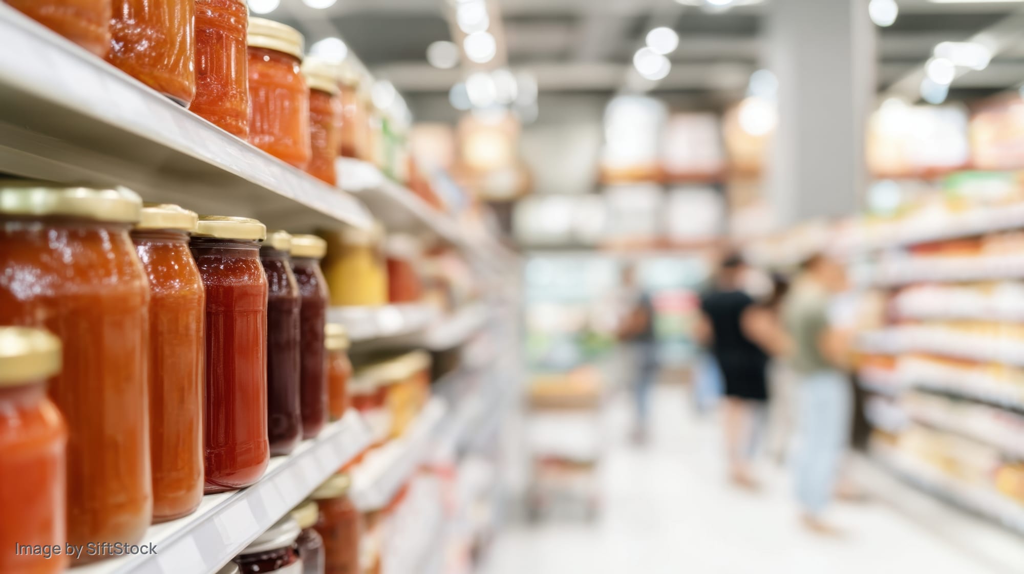 Grocery store aisle with jars of sauce and condiments on shelves, people shopping in background