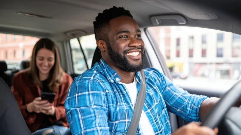 Smiling man driving a car with a woman passenger using phone in the backseat