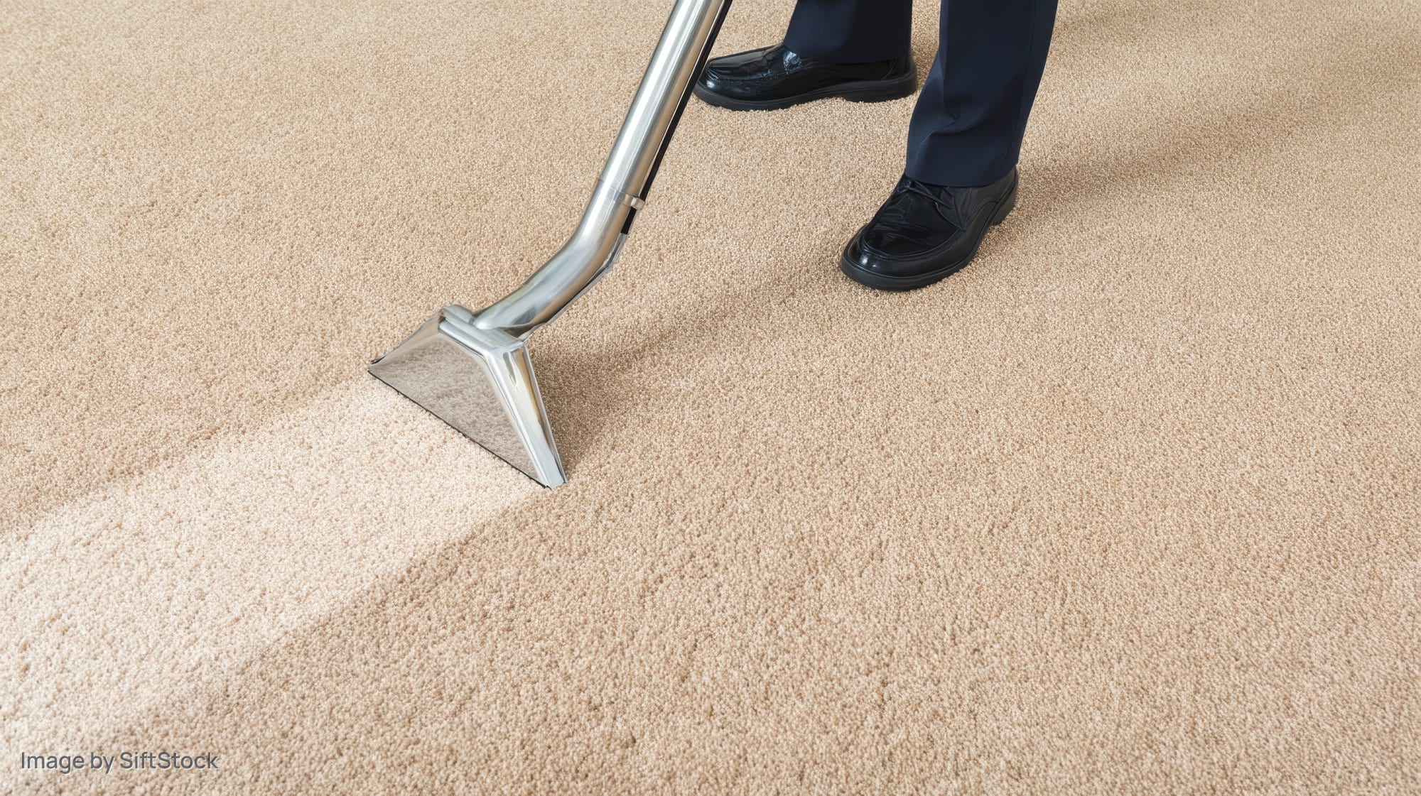 Man in suit vacuuming beige carpet in office interior