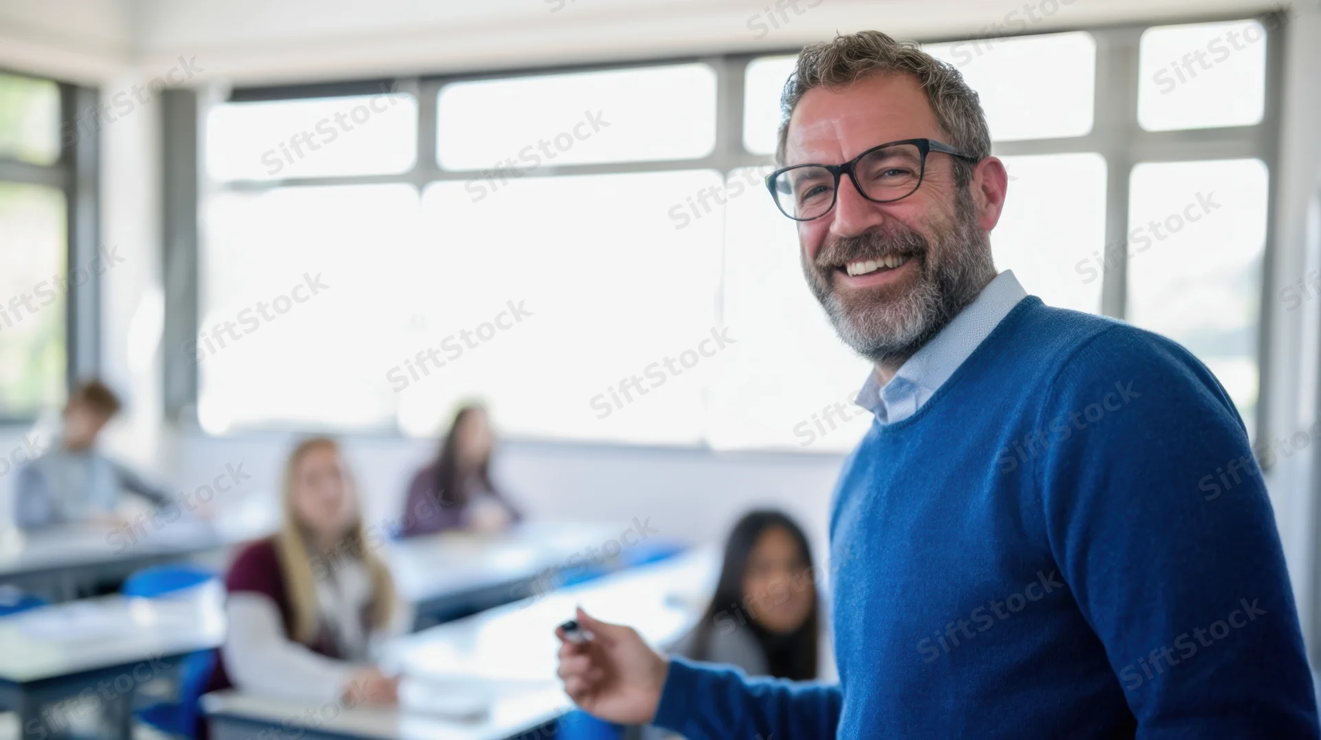 Smiling male teacher in blue sweater standing in classroom with students at desks