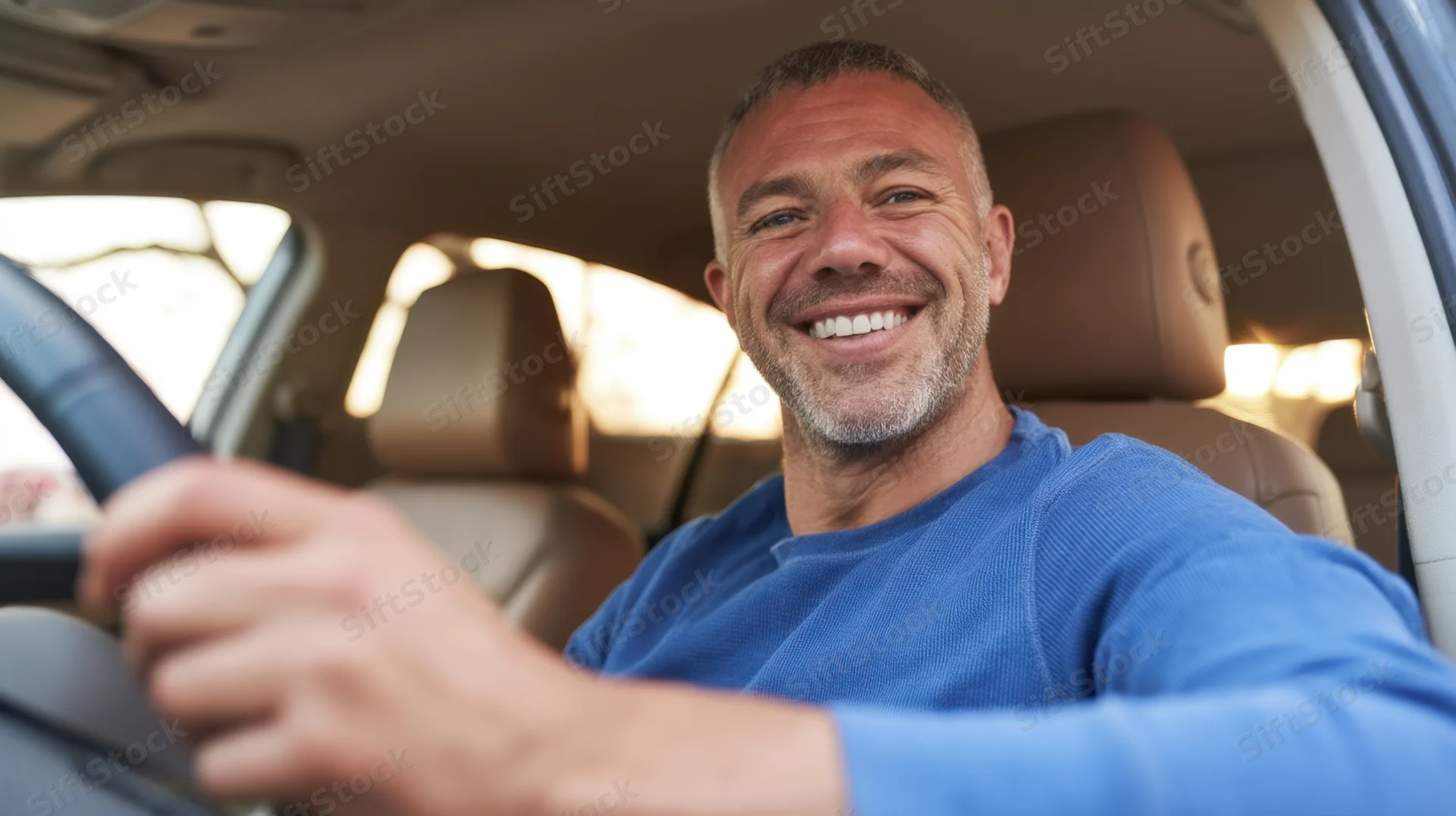 Smiling man driving a car, holding steering wheel, inside vehicle interior
