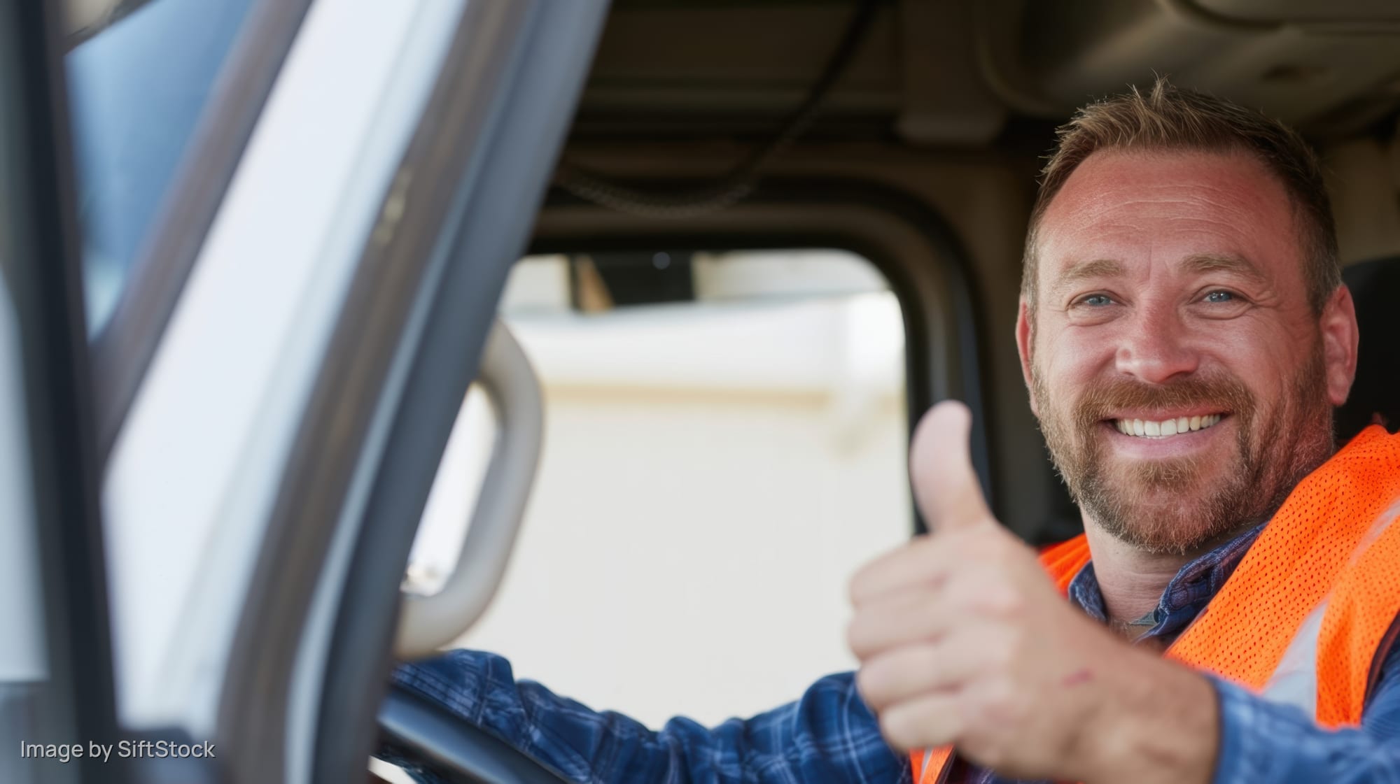 Smiling truck driver giving thumbs up from inside vehicle cab