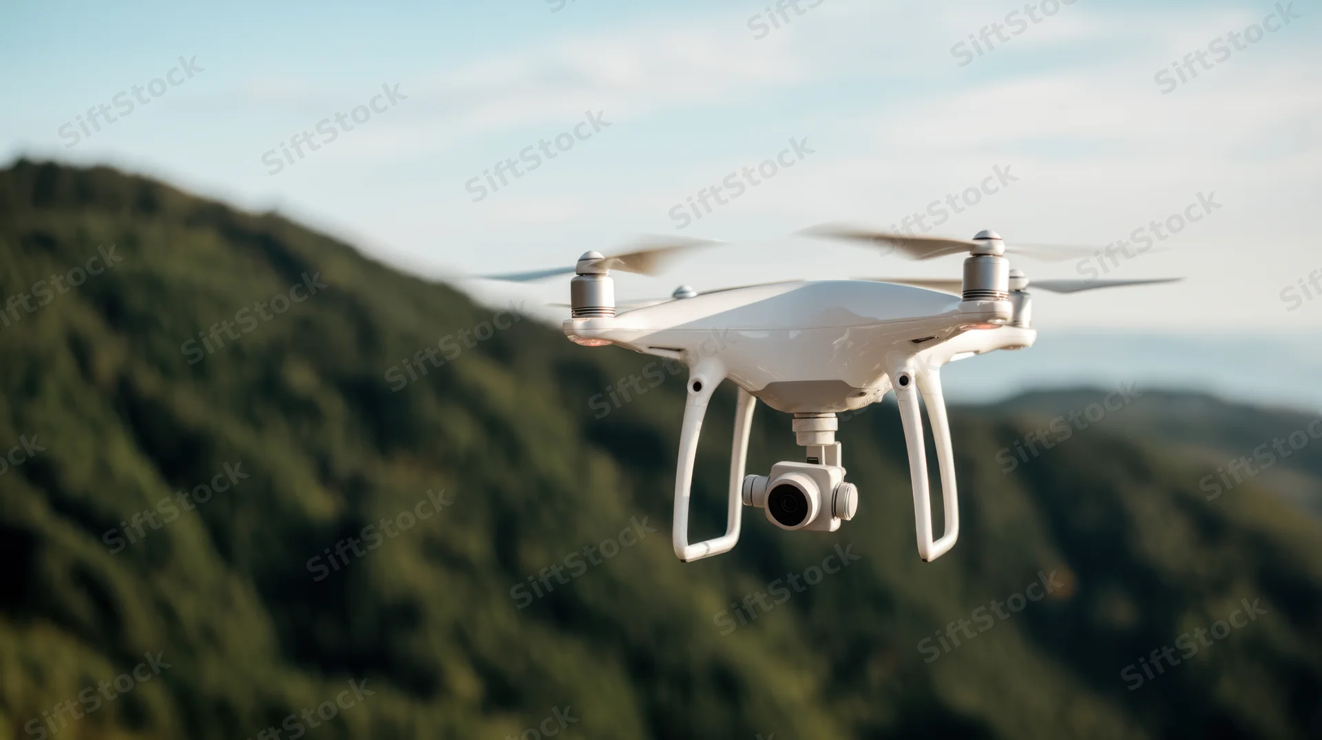 White quadcopter drone hovering in sky above forested mountains