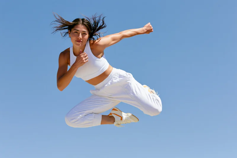 Woman jumping mid-air in white athletic wear against blue sky