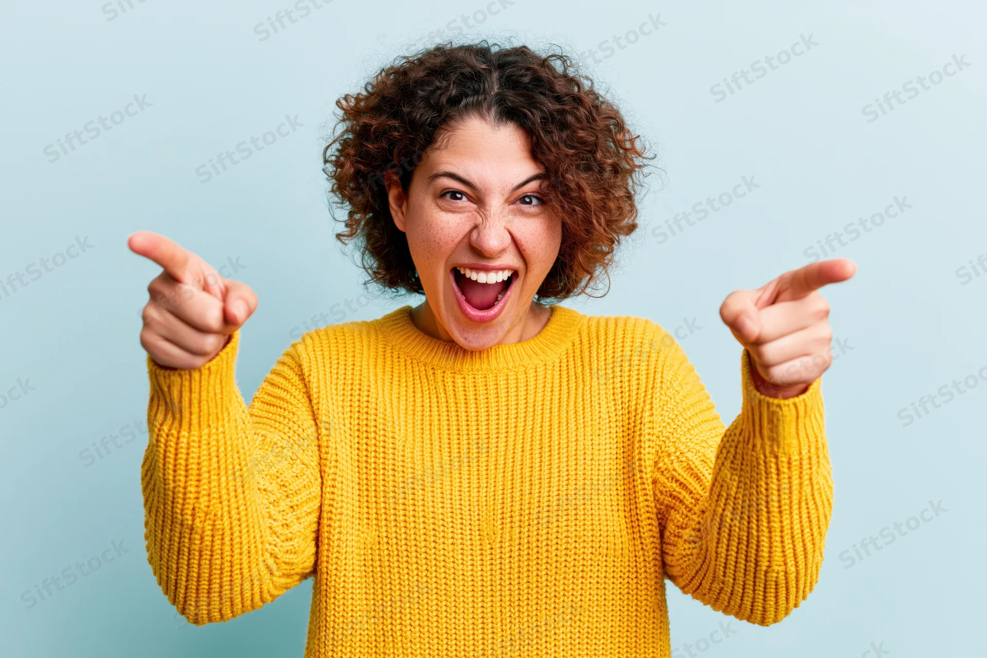 Woman in yellow knit sweater pointing excitedly with both hands against light blue background