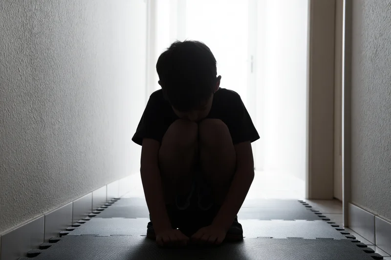 Child crouching on foam puzzle mat in dim hallway with light from doorway