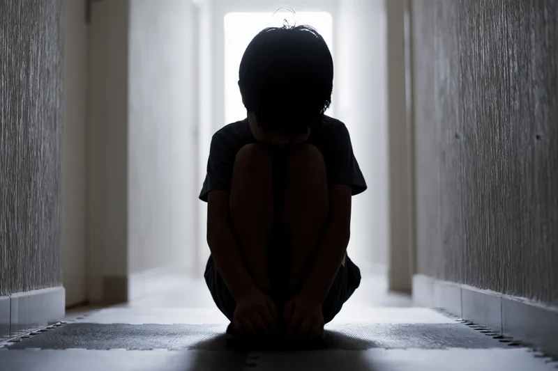 Child crouching on foam puzzle mat in dim hallway with light from doorway
