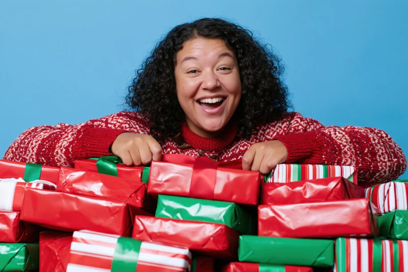 Woman smiling behind a pile of wrapped christmas gifts in red and green paper