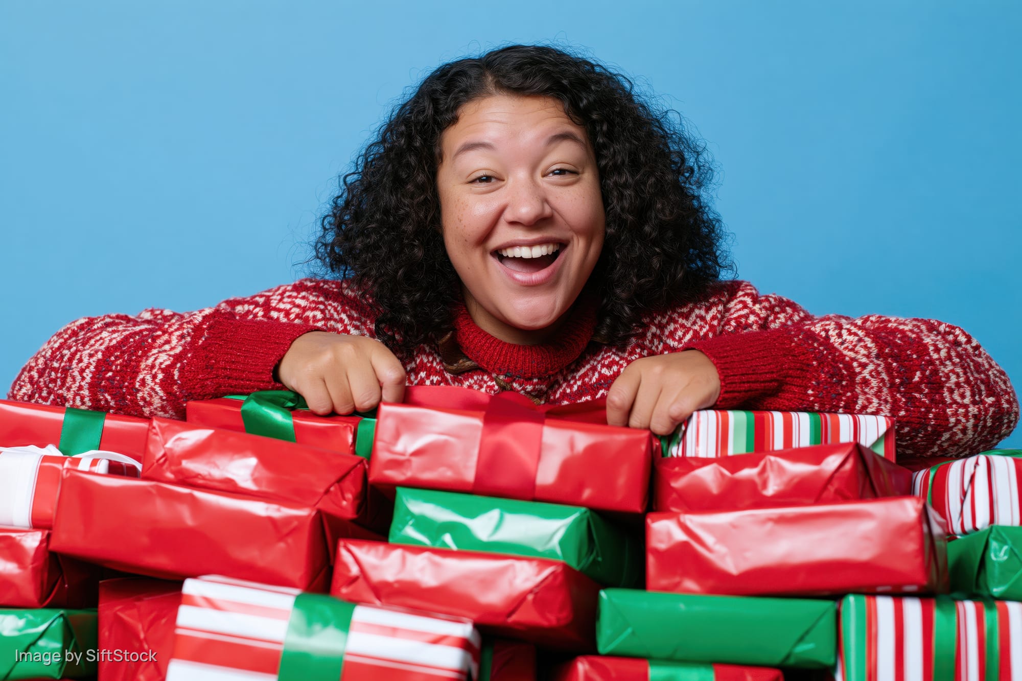 Woman smiling behind a pile of wrapped christmas gifts in red and green paper