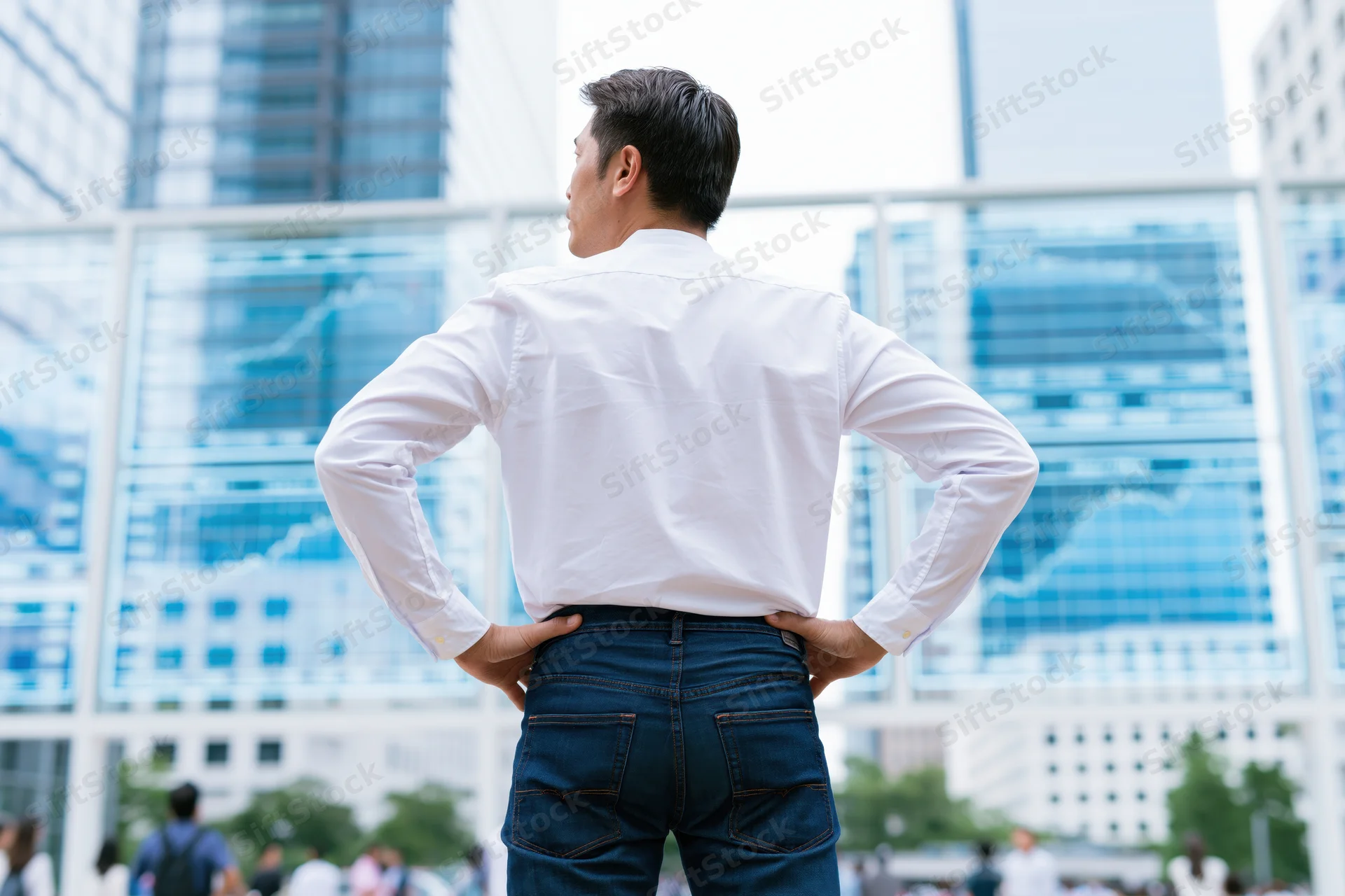 Man standing with hands on hips facing modern glass office buildings in city