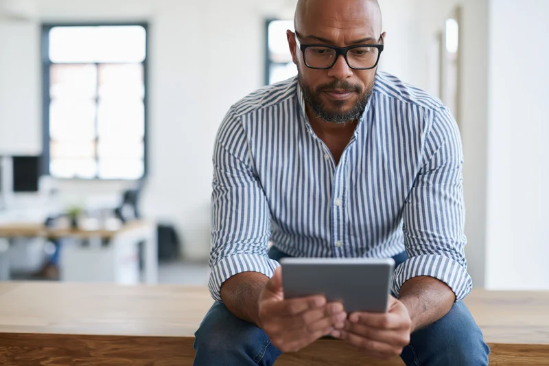 Man with glasses sitting on wooden desk using tablet in home office workspace