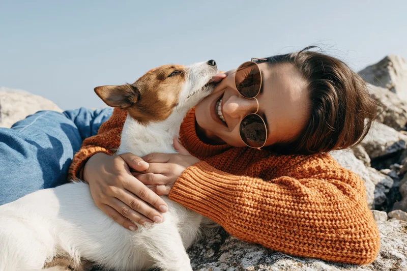 Woman smiling and hugging a jack russell dog on rocky ground outdoors