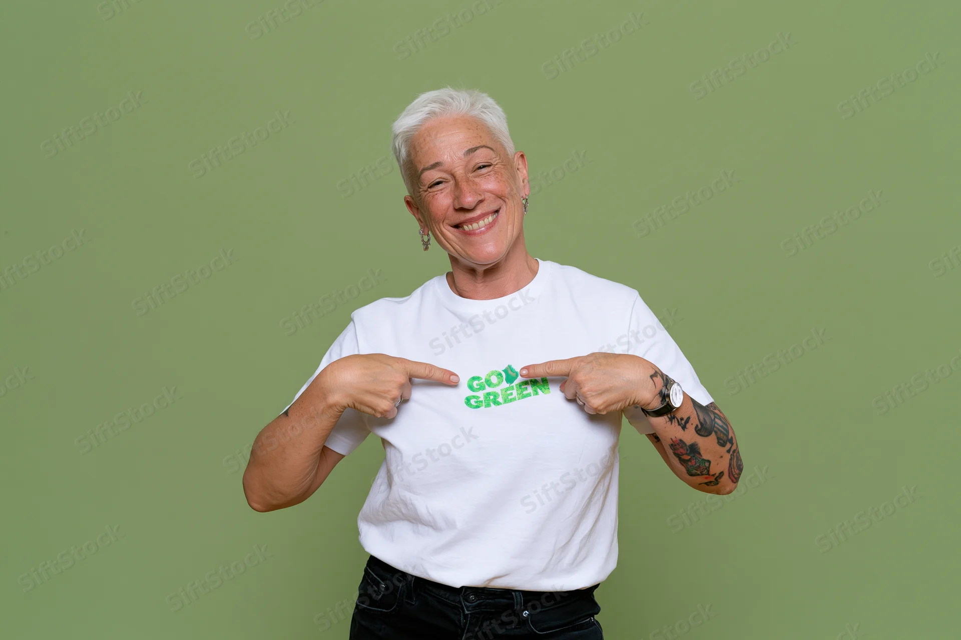 Senior woman with short white hair smiling and pointing to go green text on her white tshirt against green background