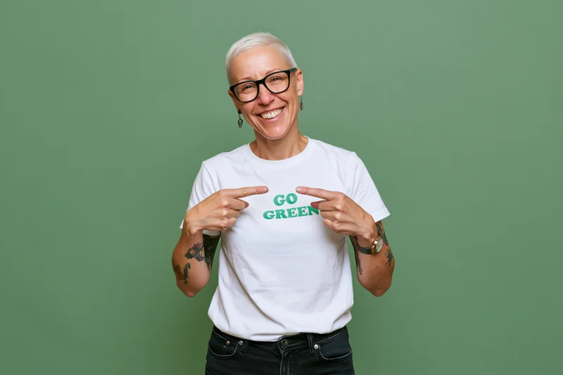 Woman smiling and pointing at go green text on her white tshirt against green background