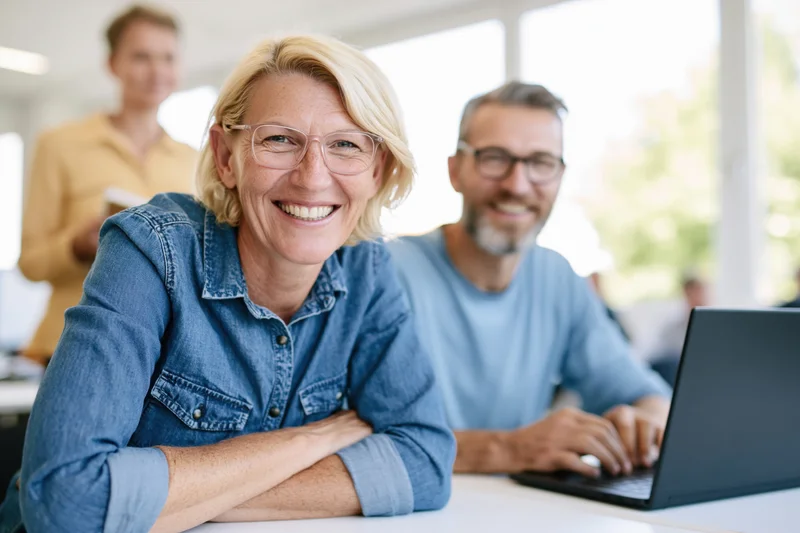 Woman smiling at camera with colleagues working at desk in office