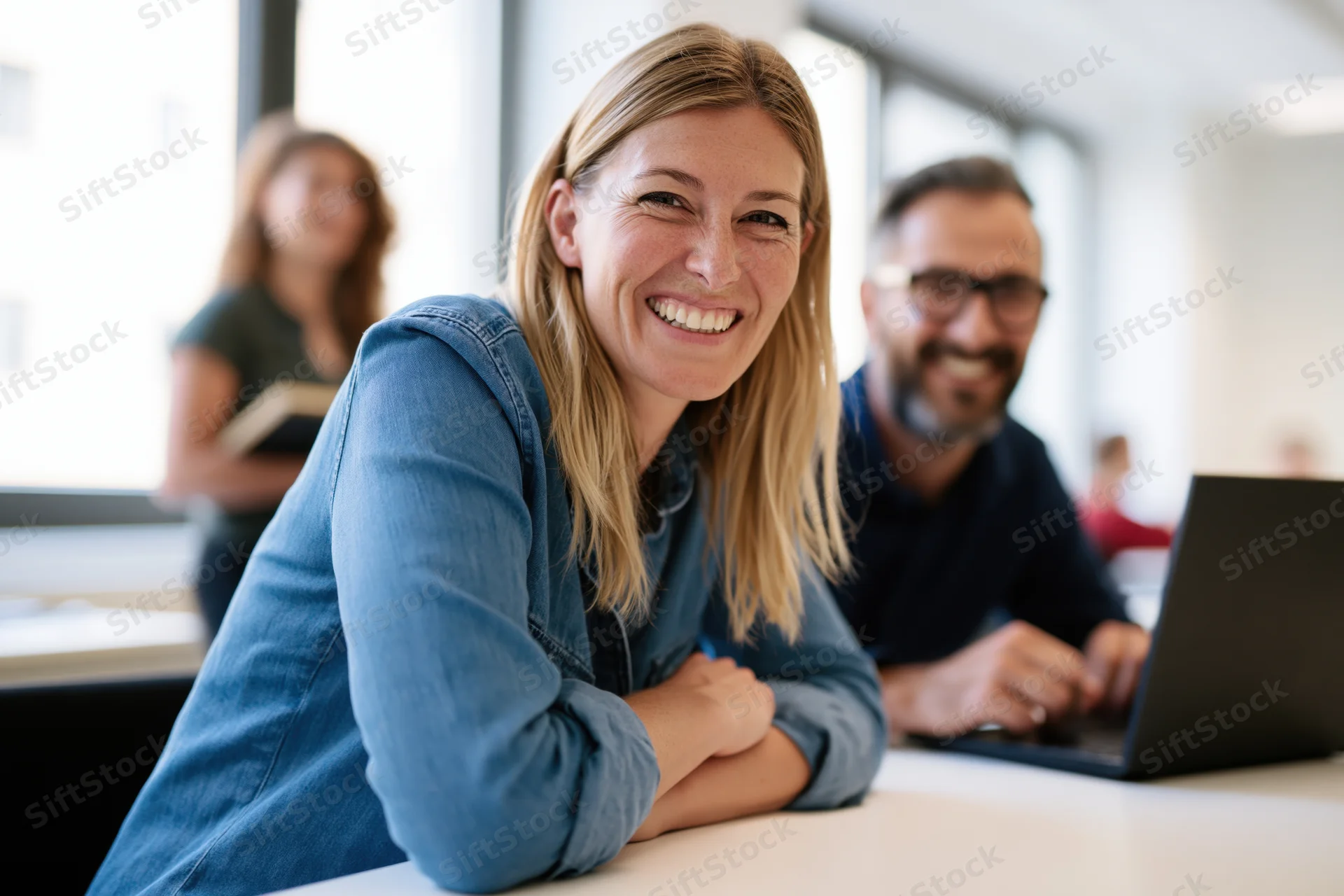 Woman smiling at camera in office with colleagues working at desks around her