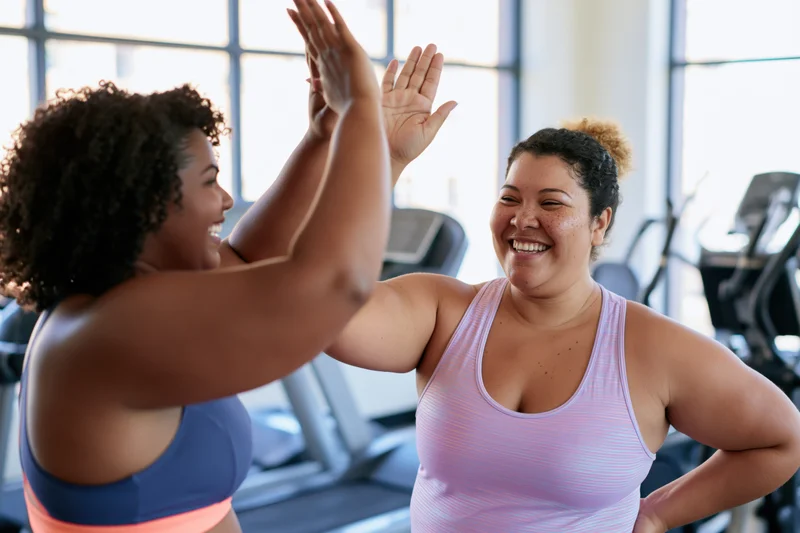 Two women in a gym giving each other a high-five while smiling during a workout