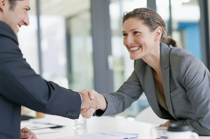 Woman and man shaking hands across a conference table in an office meeting