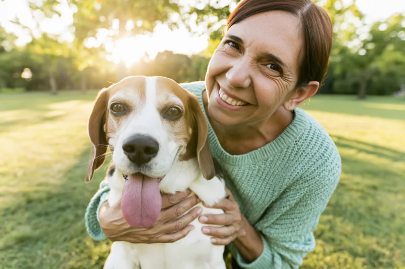Woman holding a beagle close while smiling in a sunlit park