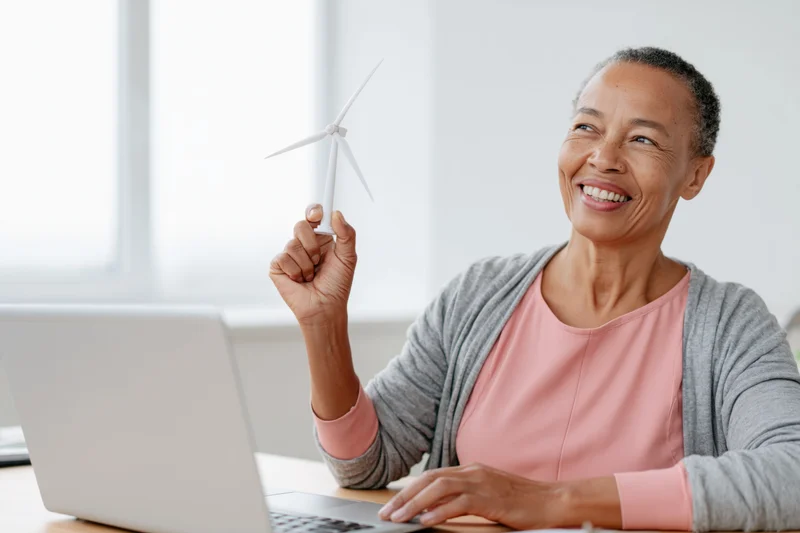 Woman holding miniature wind turbine while smiling at laptop in office