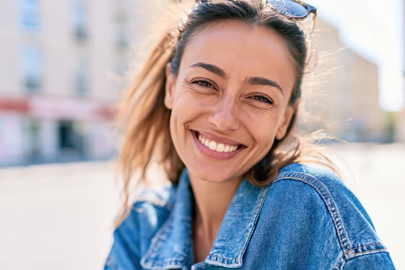 Young woman smiling with head tilted wearing denim jacket outdoors