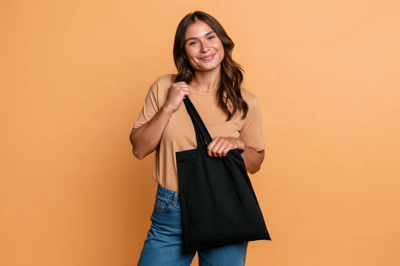 Young woman smiling while holding a black tote bag against orange background