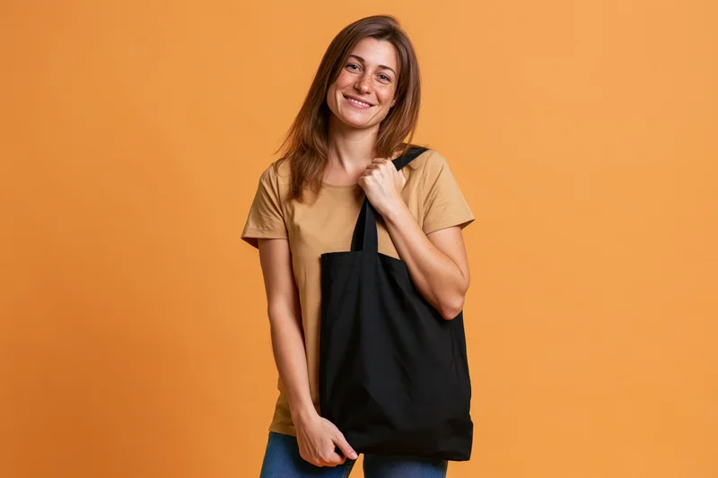 Young woman smiling while holding a black tote bag against orange background