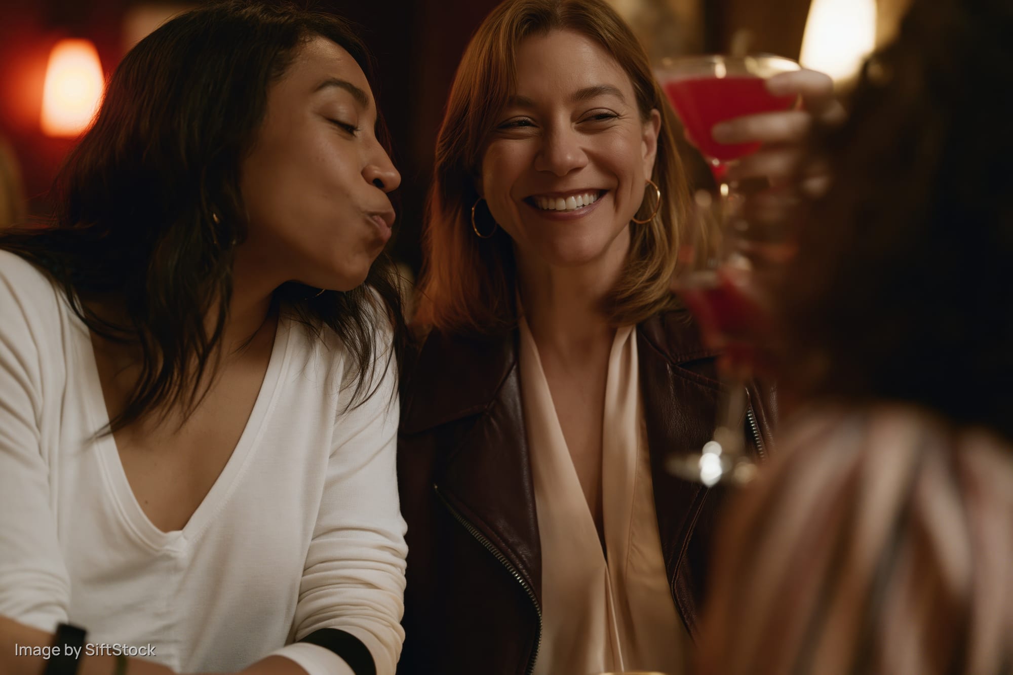 Three women toasting with cocktails in a dimly lit bar