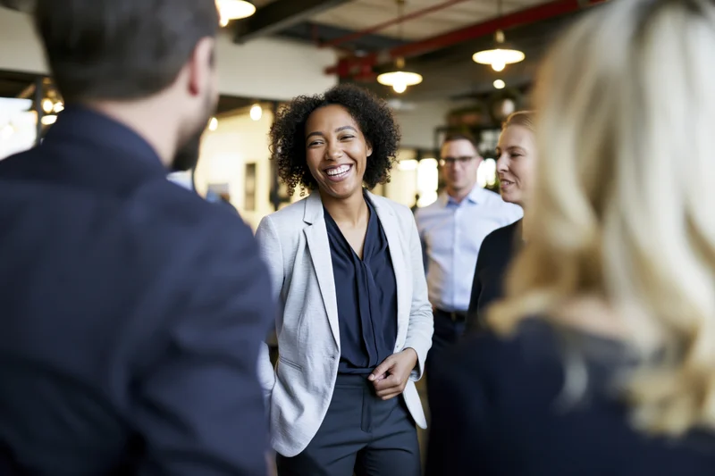 Woman smiling during office conversation with colleagues in modern open-plan workspace