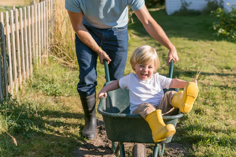 Man pushing a smiling child in a green wheelbarrow across a grassy yard