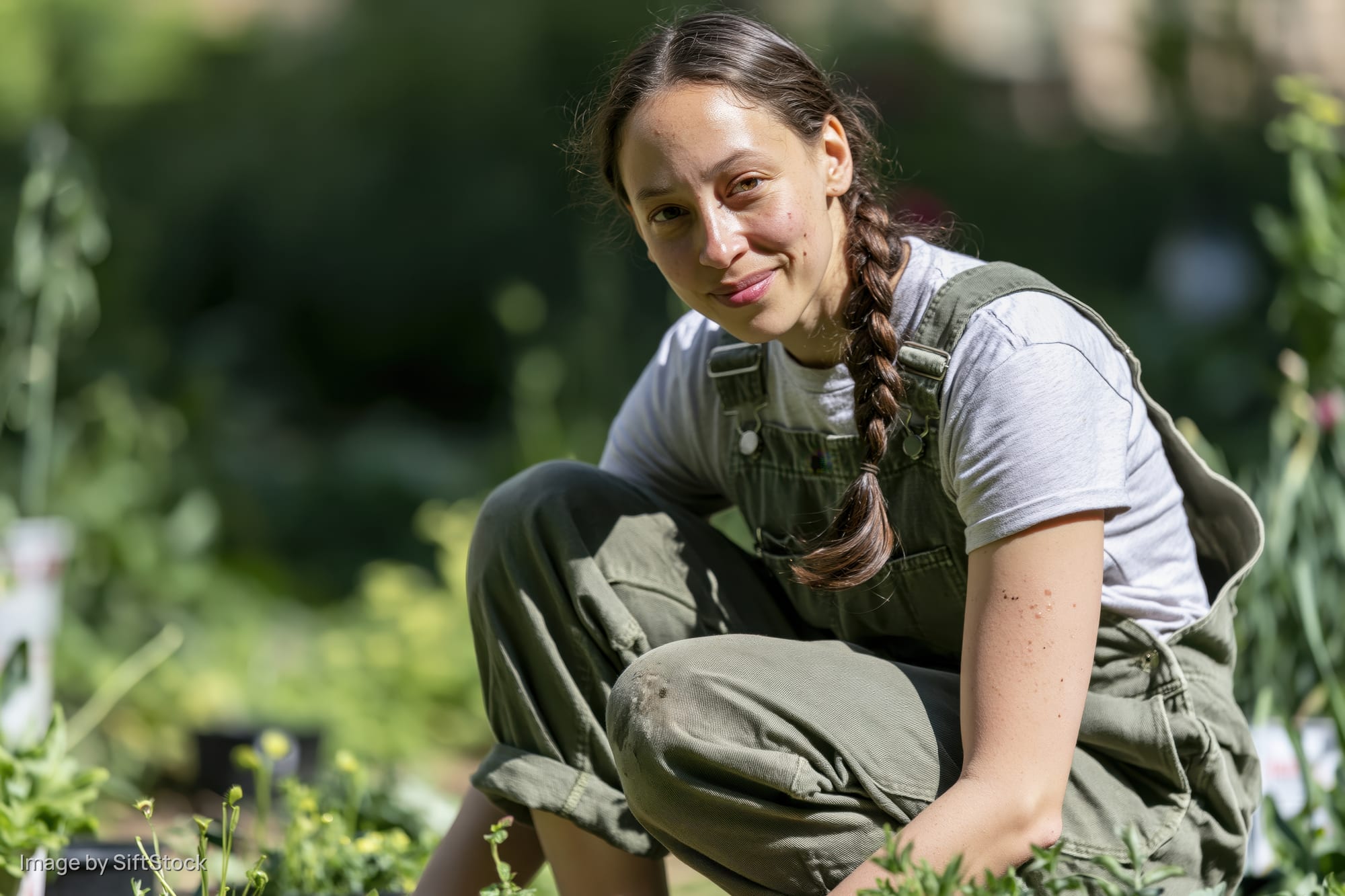 Young woman crouching in a garden surrounded by plants and greenery