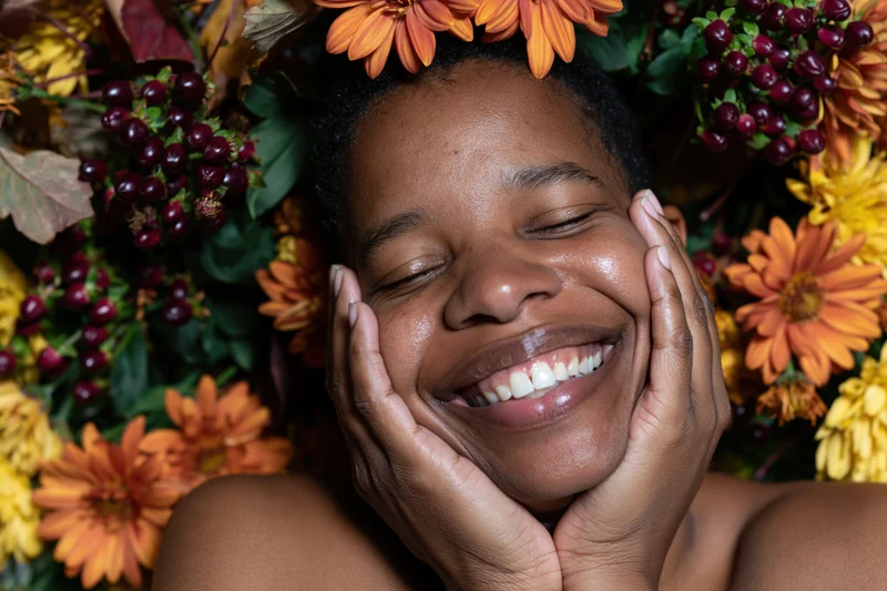 Black woman smiling with hands on face surrounded by autumn flowers and berries