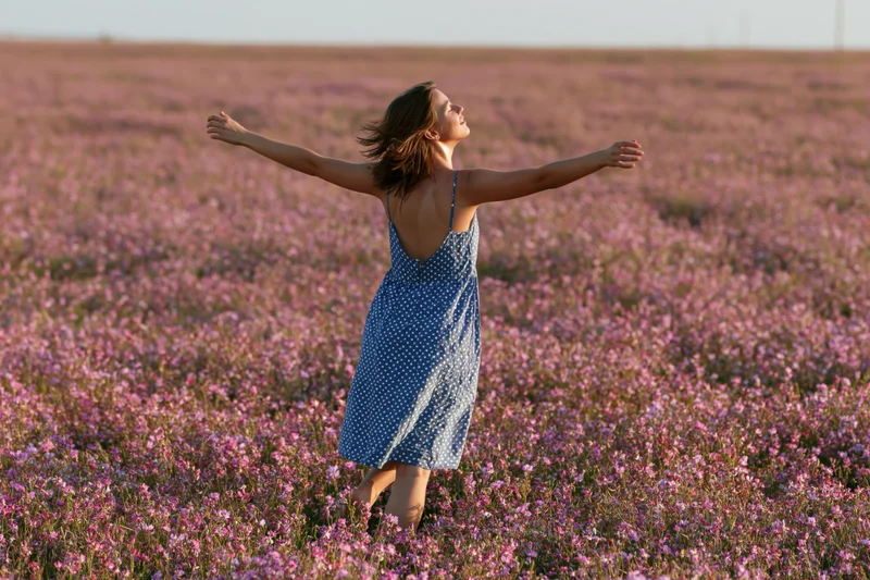 Woman with arms outstretched standing in a field of pink wildflowers during golden hour
