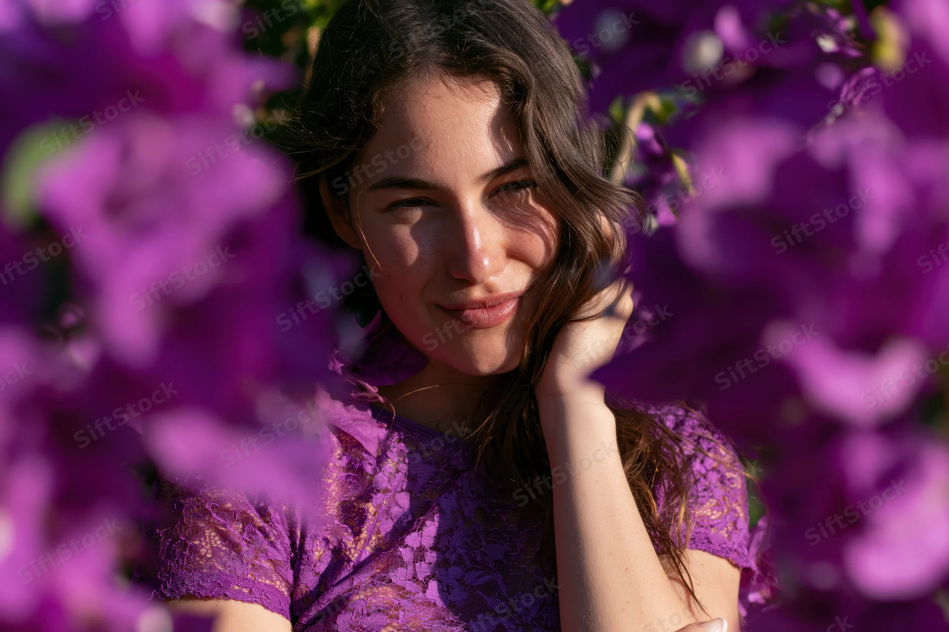 Young woman smiling through purple flowers in a garden wearing a lace dress