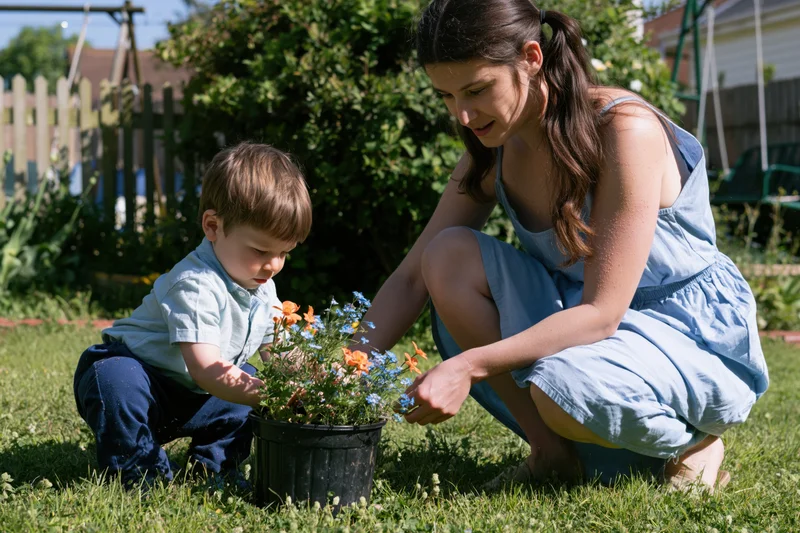 Woman and young boy crouching together in a garden tending to a potted plant with orange and blue flowers