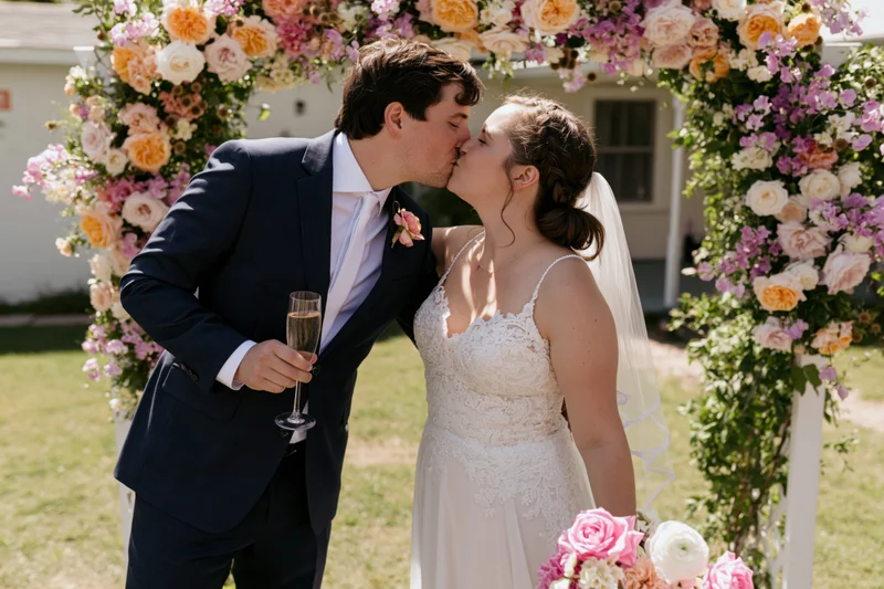 Bride and groom kissing under a colorful flower arch outdoors