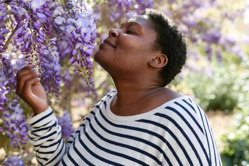 Black woman smelling purple wisteria flowers in a sunlit garden