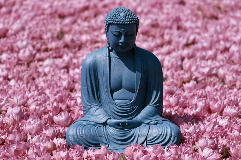 Blue buddha statue seated in meditation among pink lotus flowers in a garden
