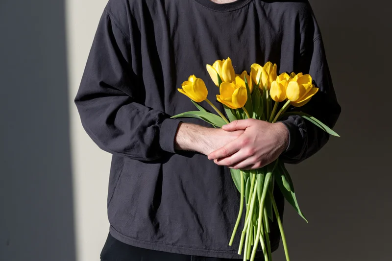 Person holding a bouquet of yellow tulips indoors with soft lighting and neutral background