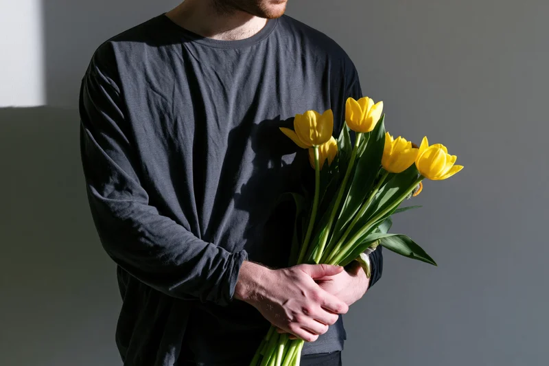 Man holding a bouquet of yellow tulips indoors against a gray wall
