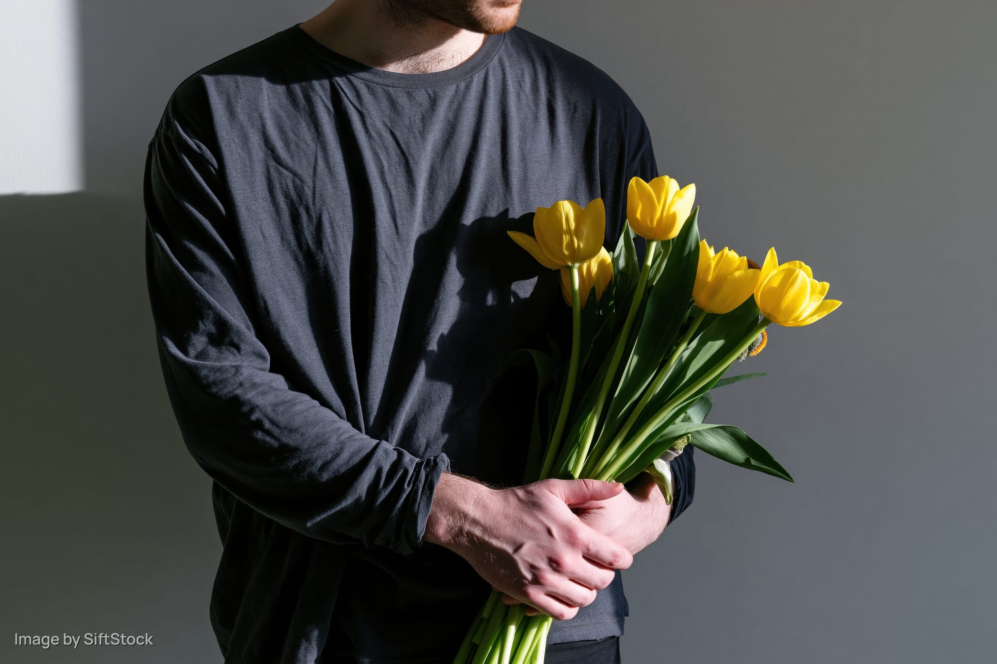 Man holding a bouquet of yellow tulips indoors against a gray wall