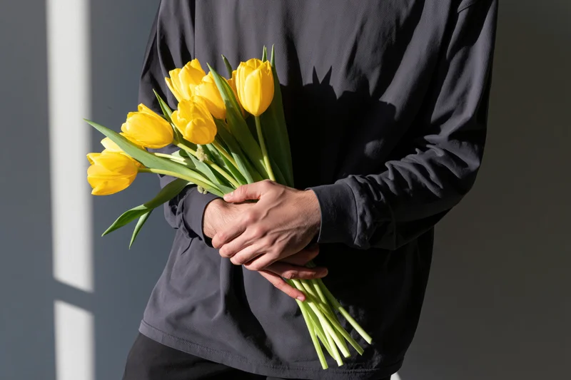Person holding a bouquet of yellow tulips against a gray wall with sunlight casting shadows