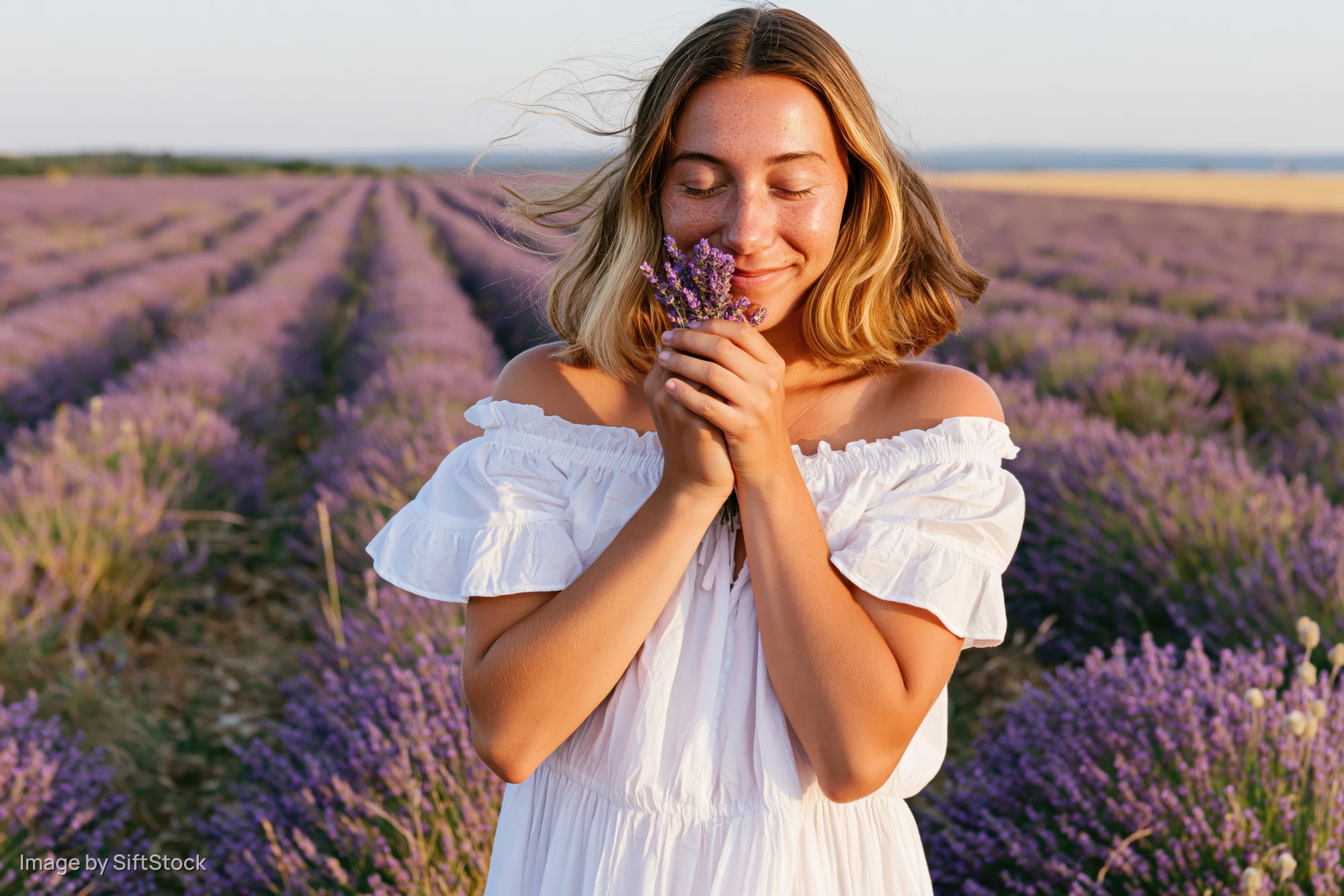 Young woman smiling while holding lavender flowers in a blooming field