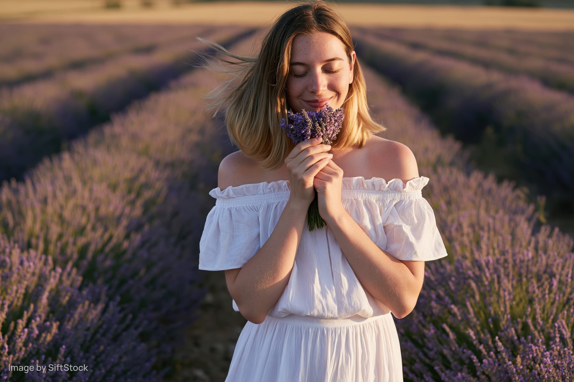 Young woman smiling with eyes closed holding lavender bouquet in a field