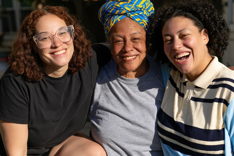 Three women smiling and laughing together outdoors in a close group portrait