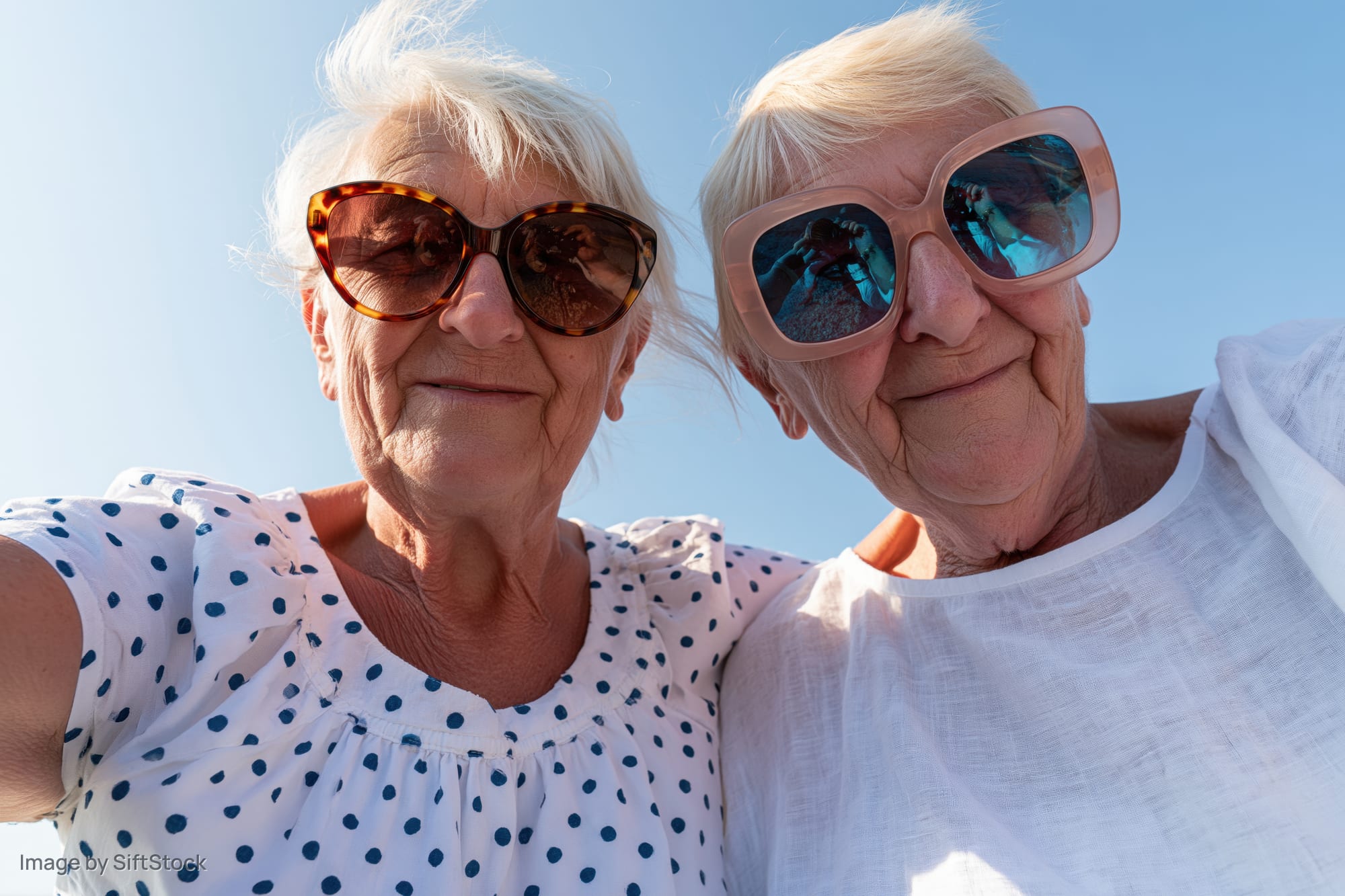 Two senior women taking a selfie outdoors wearing sunglasses and smiling