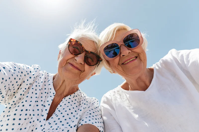 Two senior women taking a selfie outdoors under a clear blue sky