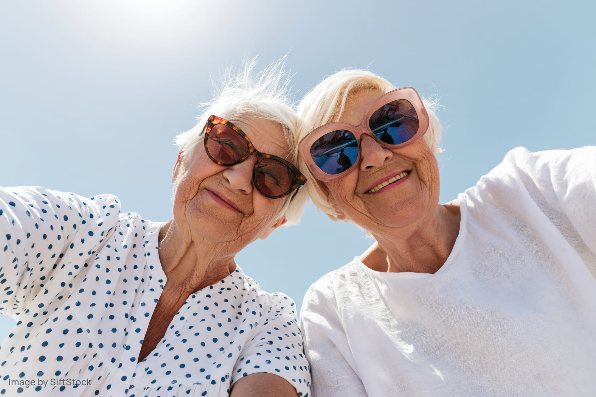 Two senior women taking a selfie outdoors under a clear blue sky