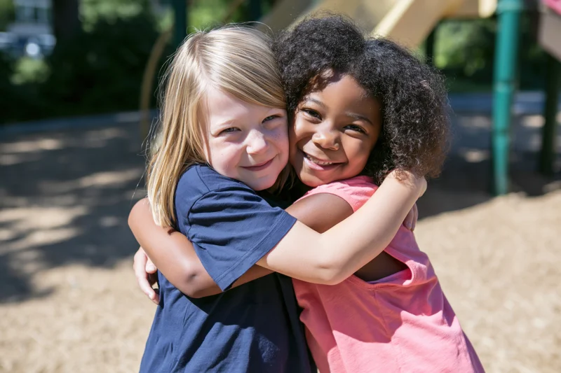 Two young girls hugging in a playground on a sunny day