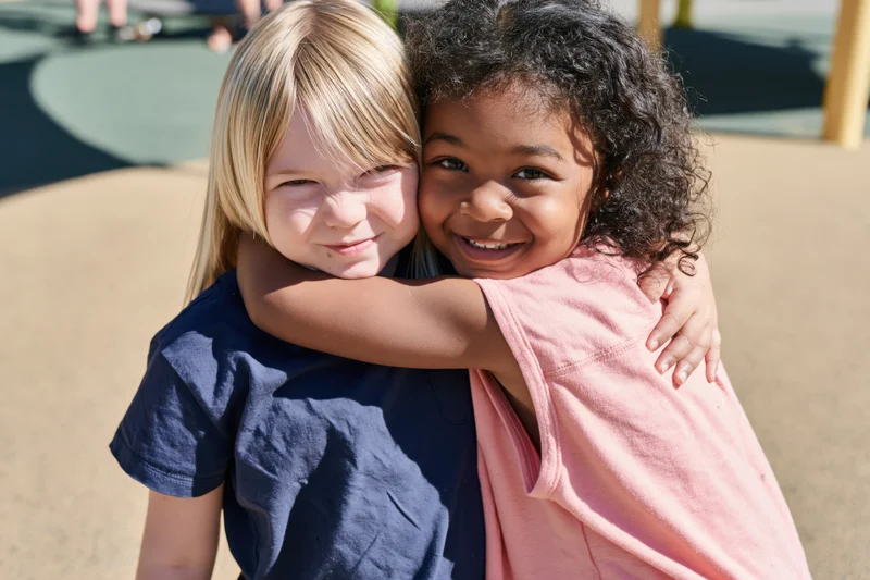 Two young girls hugging in a playground outdoors